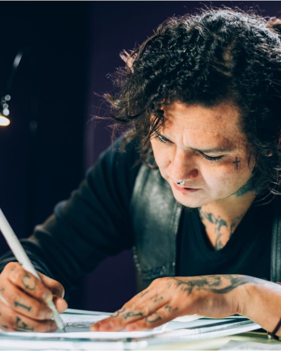 A tattoo artist drawing a design at a desk in a studio.