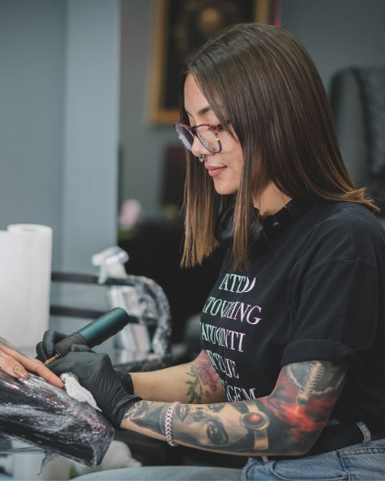 A tattoo artist working on a client's forearm in her studio.
